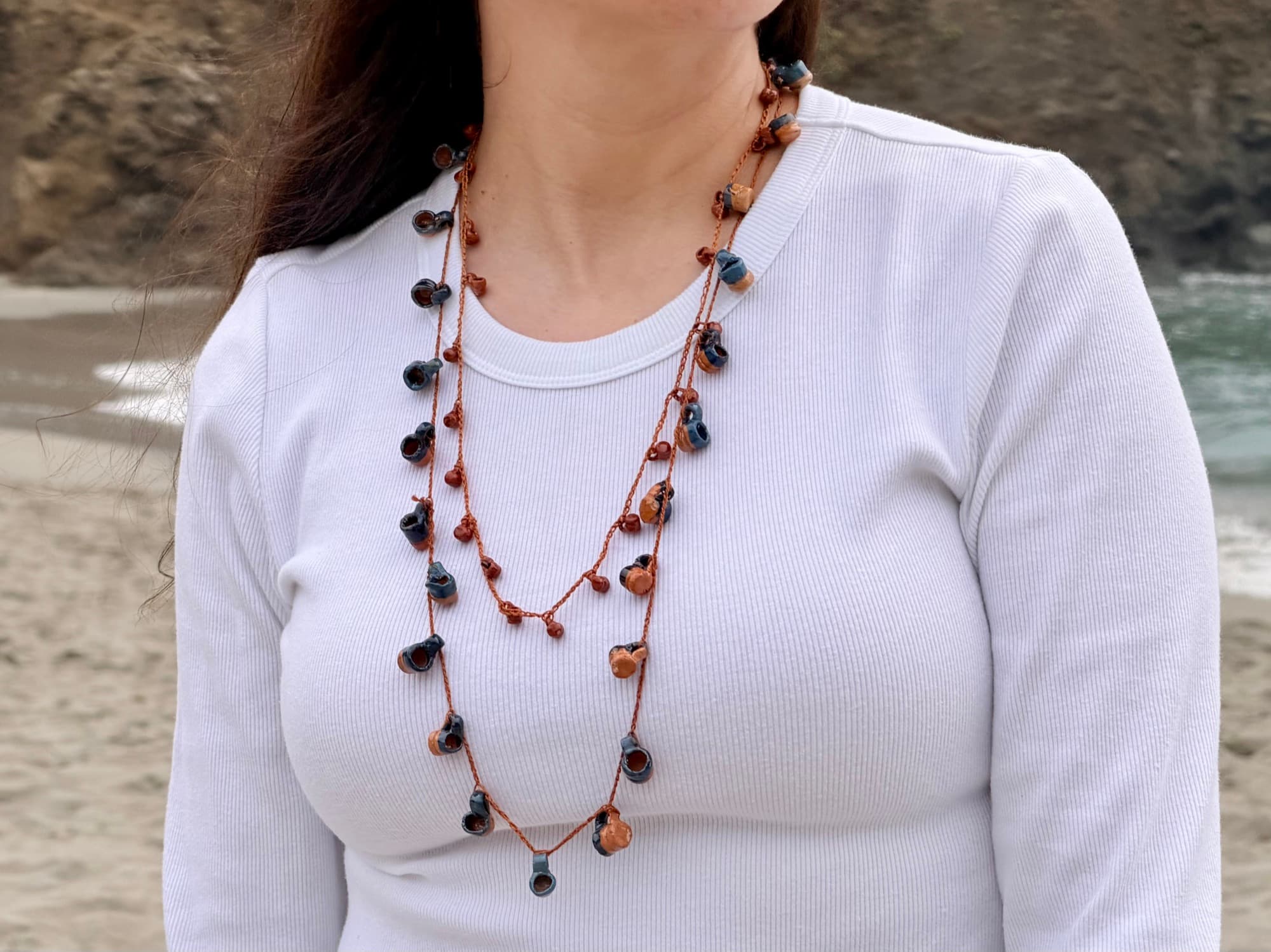 Two handmade ceramic jarrito collars layered over a white top at the beach.